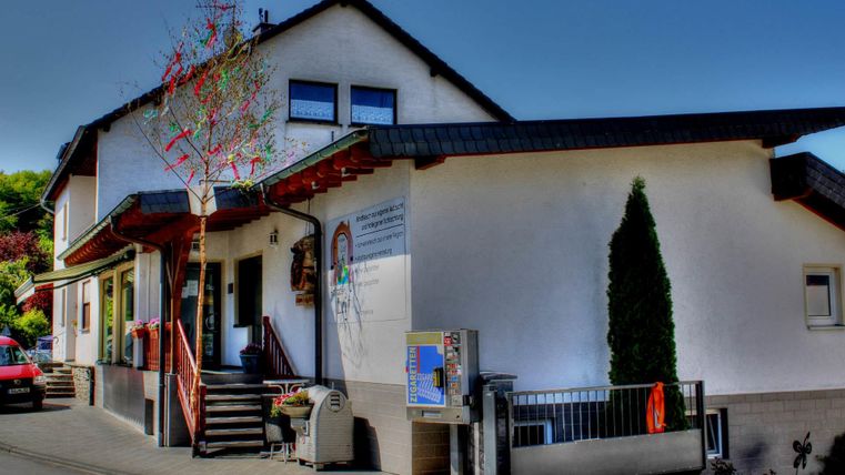 Ein modernes Gebäude mit einem freundlichen Eingang und einer grünen Hecke. Der Standort wirkt einladend und gut gepflegt.