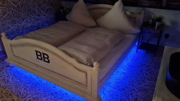 Een moderne slaapkamer met een groot bed, dat verlicht wordt door blauwe lichten. De muren zijn versierd met stro, wat een gezellige sfeer creëert.