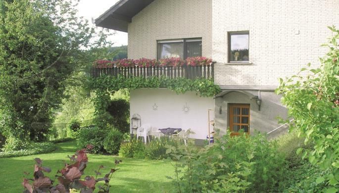 Een gezellig huis met een bloemenbalkon en een verzorgde tuin. Omringd door groene bomen en struiken straalt de scène rust uit.
