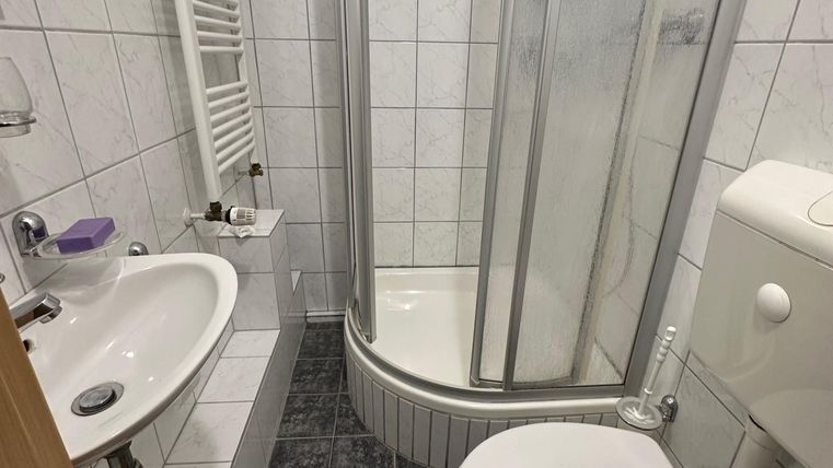 Een kleine badkamer met douche, wastafel en toilet. De muren zijn betegeld en de vloer is in een donkere tint.