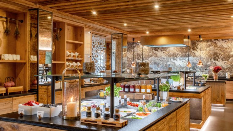 Eine moderne Küche mit Holzelementen und warmem Licht. Auf den Tischen sind frische Zutaten, Gewürze und Getränke schön angerichtet.