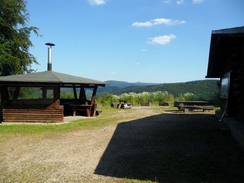 Un point de vue calme avec un coin salon couvert et vue sur les collines boisées. Le ciel est clair et l'environnement est vert et accueillant.