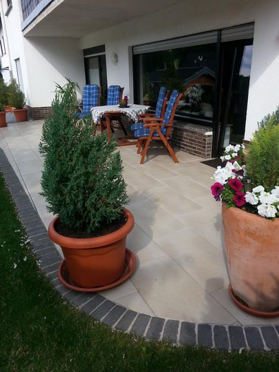 Une terrasse confortable avec deux chaises en bois et une table. À côté des chaises se trouvent des pots avec des plantes vertes et des fleurs colorées.