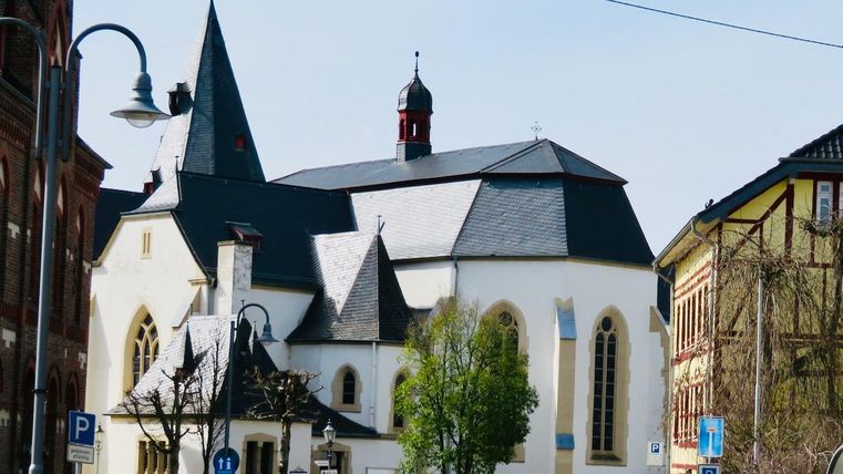 Une belle église avec un clocher marquant et des fenêtres colorées. Au premier plan, on peut voir des lampadaires et des arbres.