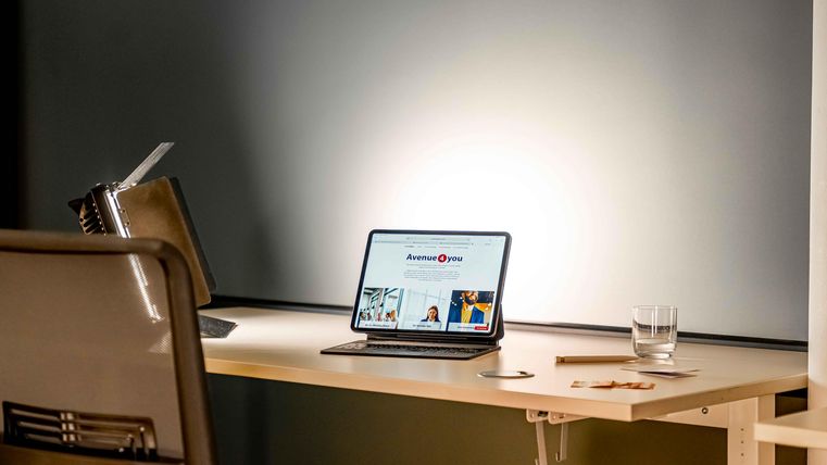 Ein moderner Schreibtisch mit einem Laptop, auf dem eine Webseite angezeigt wird. Daneben steht ein Glas Wasser und weitere Büromaterialien.