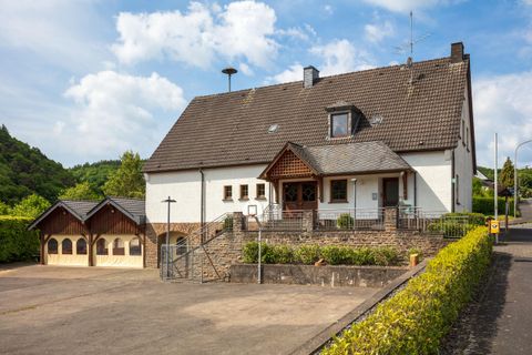 Ein großes, helles Haus mit einem Garagenanbau und einem gepflegten Vorgarten. Die Umgebung ist grün und ruhig, mit einem blauen Himmel im Hintergrund.