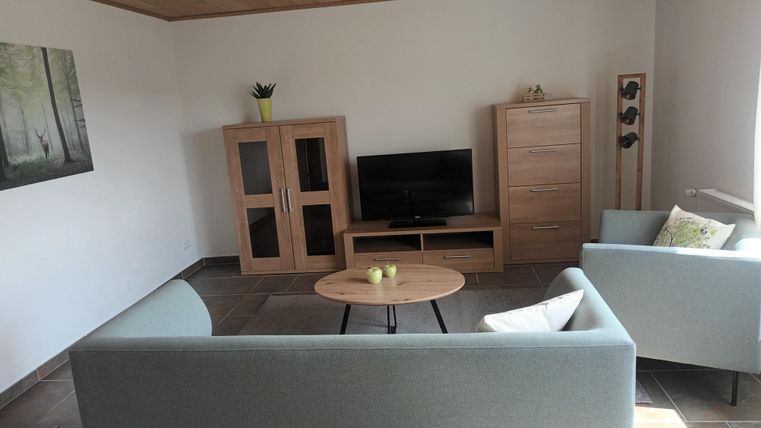 Een moderne woonkamer met twee grijze banken en een ronde tafel. In de hoek staat een televisie en een houten kast.