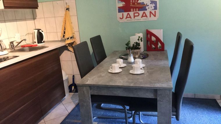 A modern dining area with a gray table and chairs. On the table are two cups and a small plant, while a kitchenette is visible in the background.