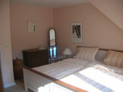 A cozy bedroom with a double bed and striped bedcovers. The room has a warm pink wall color and features a mirror as well as a dresser.