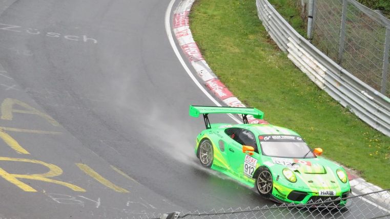 Un véhicule de course vert participe à une compétition sur un circuit sinueux. Le sol boueux génère des éclaboussures et une atmosphère excitante.