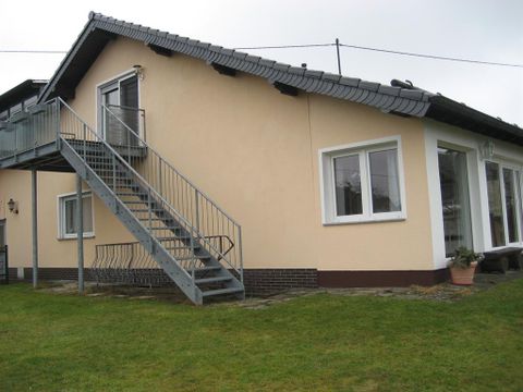 Ein modernes Haus mit einer Treppe und großen Fenstern. Die Fassade ist in einem hellen Farbton gehalten und der Garten ist gut gepflegt.