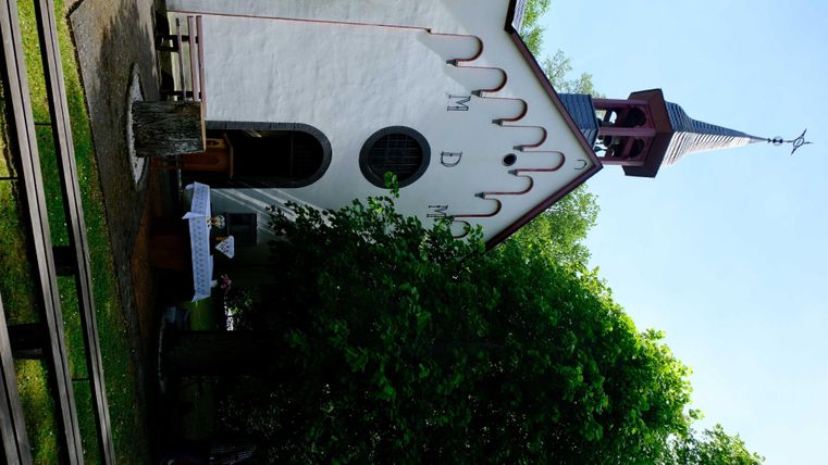 Een kleine, charmante kerk met een spitse toren. Omgeven door groene bomen en een heldere lucht.
