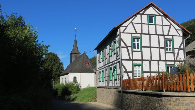 Ein malerisches Dorf mit Fachwerkhäusern und einer Kirche. Der Himmel ist klar und blau.