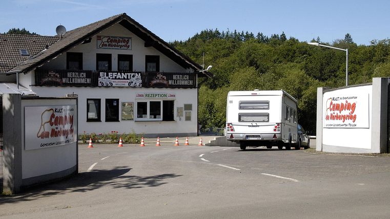 A building with a large sign and several advertising banners. In the foreground, there is a motorhome on a driveway area.