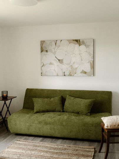 Ein elegantes Wohnzimmer mit einem grünen Sofa und einem modernen Gemälde an der Wand. Ein neutraler Teppich und ein kleiner Tisch ergänzen die gemütliche Atmosphäre.