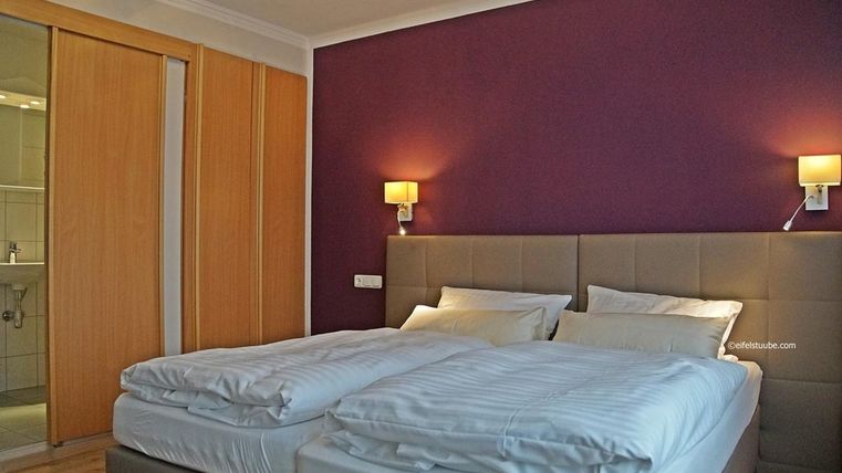 Une chambre confortable avec deux lits simples et un design moderne. Les murs sont peints dans une teinte violette et il y a un accès à la salle de bain.