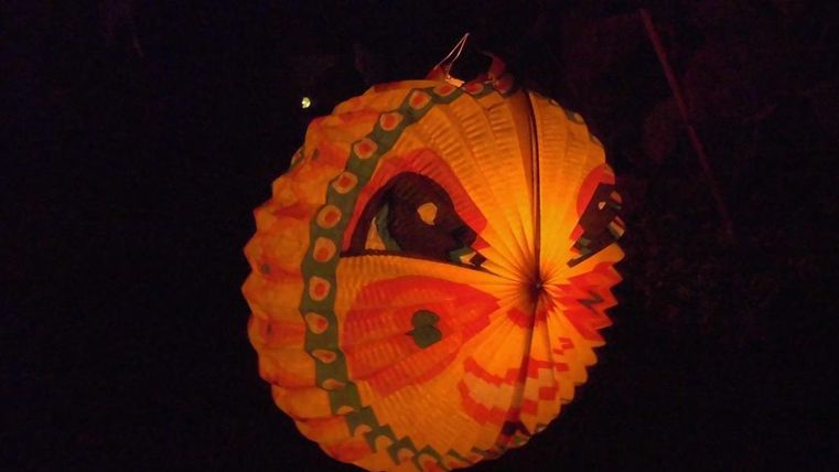 Eine leuchtende laterne in Form eines Schmetterlings hängt im Dunkeln. Sie strahlt warmes orange und gelbes Licht aus.