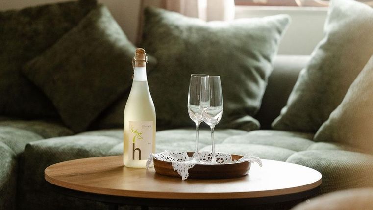 Eine Flasche mit einem Getränk steht auf einem Holztisch. Neben der Flasche stehen zwei elegante Gläser auf einem Tablett.