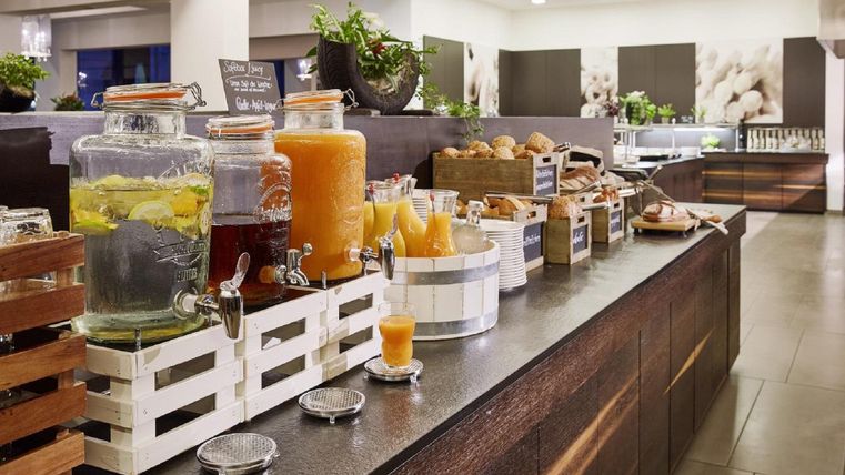 An elegant breakfast buffet with various drinks in glass jugs and fresh rolls. The counter is tastefully decorated and conveys an inviting atmosphere.