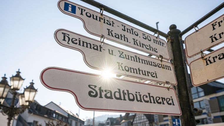 A signpost with different directions and information for tourists. In the background, buildings and city lights are visible.