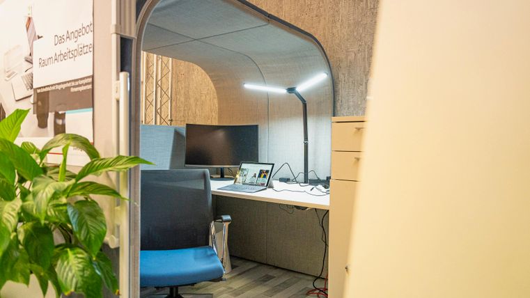 Ein moderner Arbeitsplatz mit einem Schreibtisch, einem Computer und einem bequemen Stuhl. Im Hintergrund befindet sich eine Pflanze, die für eine angenehme Atmosphäre sorgt.