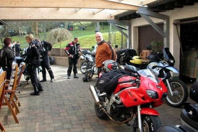 Een motorbijeenkomst onder een overdekt gebied. Verschillende mensen in motorkleding staan rondom verschillende motoren.