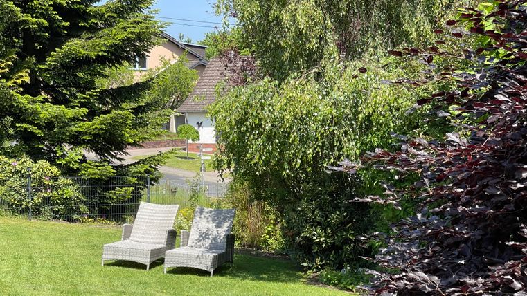 Un joli jardin avec deux chaises longues. Entouré d'arbres et de buissons colorés.