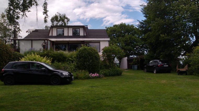 A beautiful house surrounded by green grass and trees. Two cars can be seen in the garden.