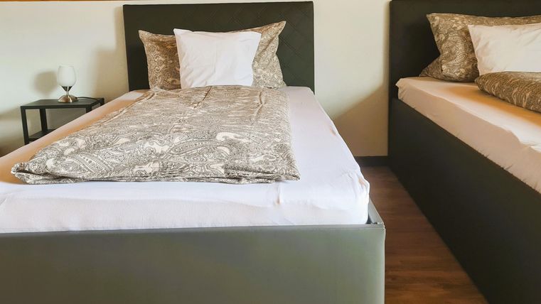 Two single beds in a modern room. The beds are decorated with gray blankets and pillows.