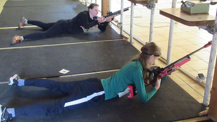 Zwei Personen liegen auf dem Boden und trainieren mit Gewehren. Sie konzentrieren sich auf das Schießen in einer Trainingsumgebung.