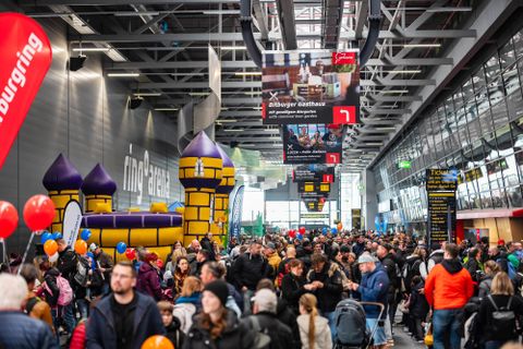 Eine große Menschenmenge in einer Halle mit einem großen, bunten Hüpfburg im Hintergrund. Die Atmosphäre ist lebhaft mit vielen Familien und Kindern.