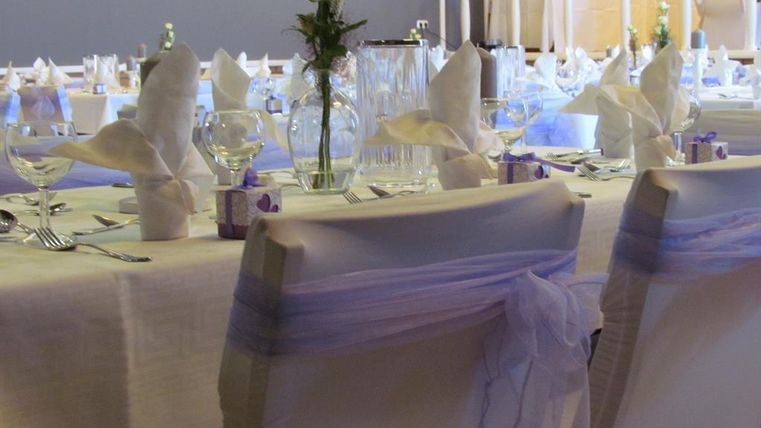 A festively set table with white napkins and elegant glasses. Beautifully decorated with a flower and lilac-colored accents.