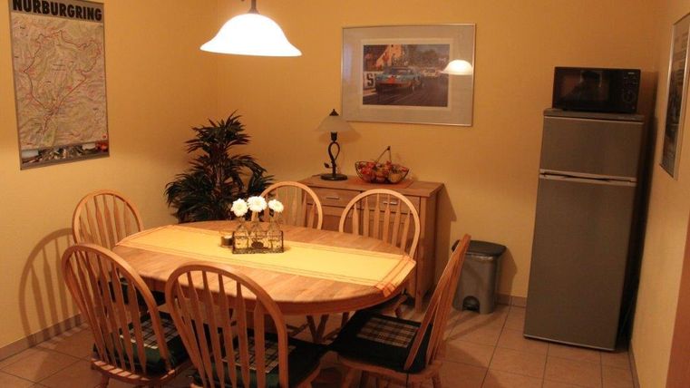 A cozy dining area with a round wooden table and eight chairs. The walls are painted in warm yellow tones and there is a refrigerator and a microwave in the corner.