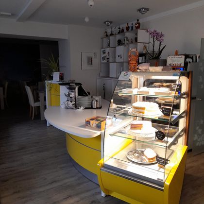 A modern café with a yellow sales counter. The display case shows a selection of cakes and tarts.