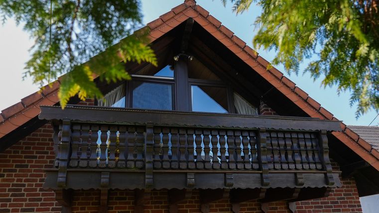 Een traditioneel huis met een houten balkon en een rood pannendak. De ramen zijn groot en laten veel licht binnen.