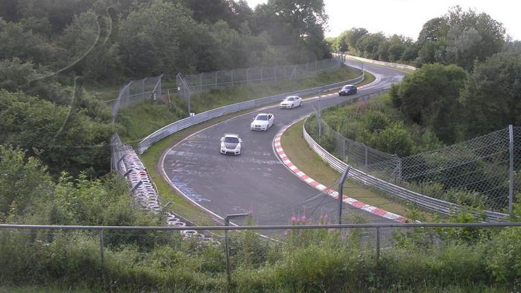 Een bochtige racebaan omringd door bomen. Meerdere auto's rijden op de baan.