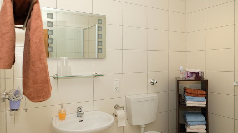 Une salle de bain moderne avec un petit lavabo, un miroir et des toilettes. Des serviettes et des tissus pliés sont soigneusement rangés.