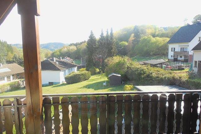 Une scène rurale paisible avec de l'herbe verte et quelques arbres dispersés. À l'arrière-plan, on peut voir quelques maisons et des collines.