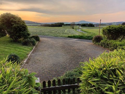 A paved path winds through a green landscape with gentle hills. The sky is tinged in warm colors of the sunset.