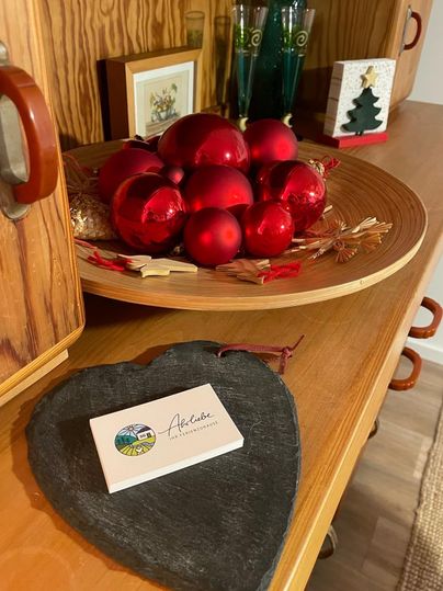 Une table décorative avec un plateau en bois, sur lequel se trouvent des boules de Noël rouges. À côté se trouve un dessous de verre en forme de cœur avec une carte.