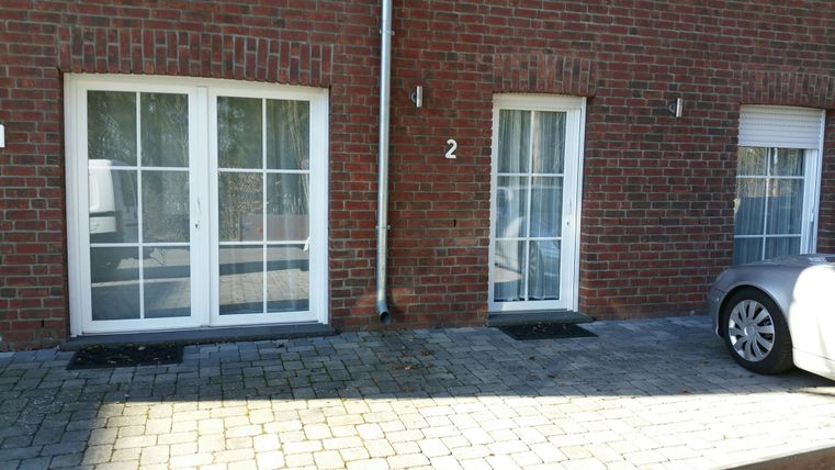 Two entrances to a well-lit building, surrounded by brick walls. The path is paved with stones and a car is parked nearby.