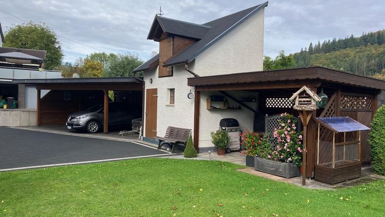 Une petite maison bien entretenue avec un garage et un beau jardin. Au premier plan, il y a des fleurs et des pelouses.