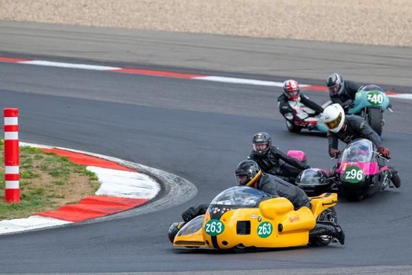 Ein spannendes Motorradrennen mit Seitenwagen auf einer Rennstrecke. Mehrere Fahrer nehmen eine Kurve im Wettkampf.