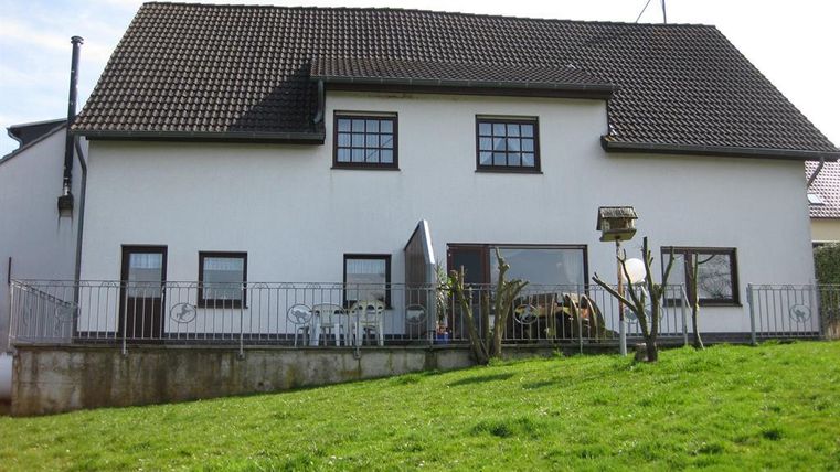 Ein großes, zweigeschossiges Haus mit einem Satteldach und vielen Fenstern. Der Garten ist grün und gepflegt, ideal für die Freizeit.