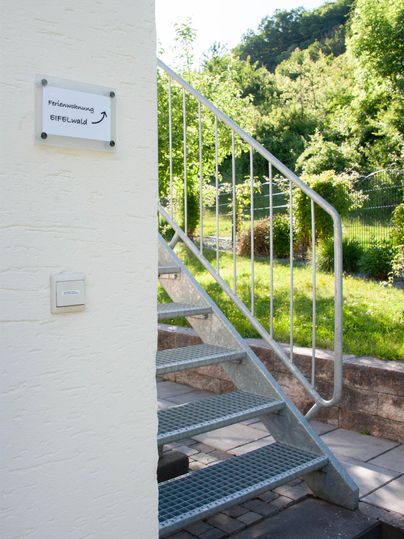 A metal staircase leads upwards. In the background, there are green trees and a meadow.