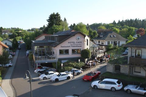 Ein Hotelcafé mit einem Restaurant in einer ruhigen Wohngegend. Autos parken entlang der Straße und Gäste sitzen draußen.