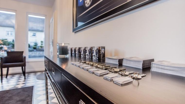 Ein eleganter Empfangsbereich mit einem schwarzen Tisch. Auf dem Tisch liegen Schlüssel und Handouts, während im Hintergrund ein Stuhl und Fenster sichtbar sind.