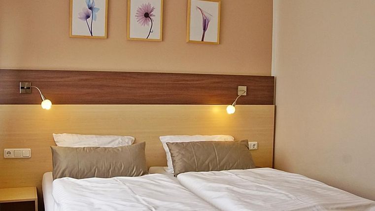 Une chambre confortable avec deux lits et de doux coussins. Trois tableaux de fleurs sont accrochés au mur.