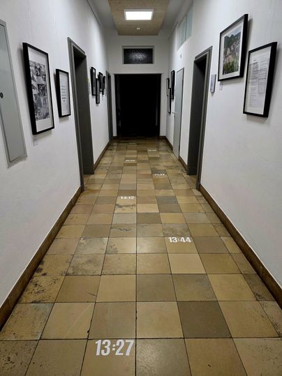 A long hallway with light walls and a tiled floor. Pictures hang on the walls, and numbers are printed on the floor.