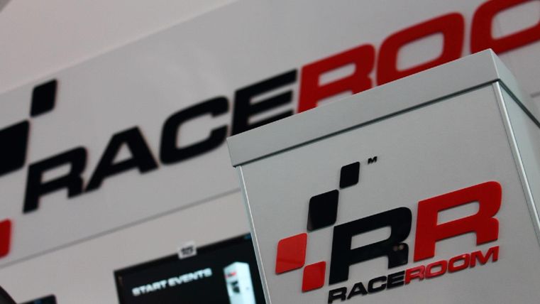 Ein Stand von RaceRoom mit einem klaren Fokus auf Motorsport und Rennsimulationen. Das Logo ist prominent auf dem Tisch und der Wand dargestellt.